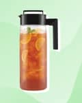 Pitcher of iced tea with lemon slices and mint, black handle, on a green background.