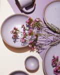 Speckled lavender ceramic dishes with pink flowers on a purple surface.