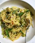Spaghetti with creamy zucchini sauce, garnished with fresh basil and red pepper flakes in a white bowl.