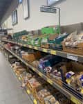 Grocery store aisle with shelves of assorted bagels and rolls in various packaging.