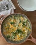 Broccoli and cheddar risotto in a pink pan on a wooden table with forks and a napkin nearby.