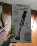 Vitamix Immersion Blender box held over a wooden floor, next to a teal chair and a wooden table.