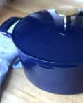 Blue enameled cast iron Dutch oven with a brass knob on a wooden countertop.