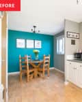 Wood dining table and chairs in turquoise room seen from gray kitchen with white cabinetry.