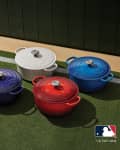 Four Le Creuset Dutch ovens in red, blue, white, and navy on grass, featuring MLB team logos.