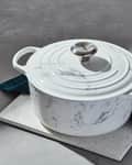 Marble-patterned Dutch oven with lid on a speckled trivet, next to a teal cloth.