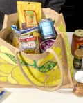 angled shot of an assortment of trader joe's groceries in a yellow and tan trader joe's tote bag - and some of the groceries are scattered around the bag on the counter.