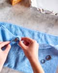 Hands cleaning a ring with a blue cloth on a marble surface, with other rings nearby.