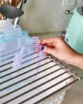 A person placing a container lid into a drying rack with other lids