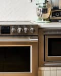 Stainless steel oven with control knobs, surrounded by white cabinets, a mint green mixer, and a toaster.