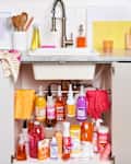 Under-sink storage with cleaning supplies, rubber gloves, and towels in a kitchen with a marble countertop and faucet.