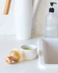Kitchen sink with a soap dispenser, wooden dish brush, and white pitcher on a tiled backsplash.