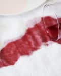 Spilled red wine on white tablecloth with overturned glass, near a fork and napkin.