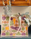 Reusable grocery bag with vegetable prints on a kitchen counter, filled with eucalyptus branches.