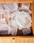 Open kitchen drawer filled with various sizes of clear plastic food storage containers.