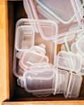 A wooden drawer filled with various clear plastic food storage containers in different sizes and colors.