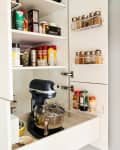 A black KitchenAid mixer inside a pantry filled with spices and cooking spray
