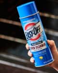 Hand holding a can of Easy-Off Oven Cleaner in front of open oven