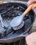 Cleaning a cast iron skillet with a brush in the sink