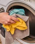 Hand placing colorful clothes into a front-loading washing machine.