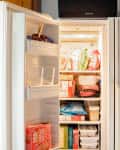 Refrigerator, with freezer door opened. Food in freezer has been neatly organized. On the fridge door the freezer inventory checklist is hanging.