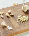 Whole garlic cloves, individual peeled cloves, and a small pile of pressed garlic on a cutting board