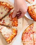 someone taking a piece of cheese frozen pizza with other pizza around