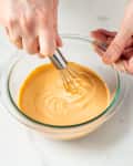 Someone whisking sauce in glass bowl.