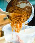 Someone scooping spaghetti leftovers into food storage container.