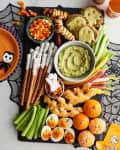 Festive Halloween snack board with mummy pretzels, guacamole, candy corn, and ghost-shaped cheese on crackers.