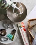 Baking tools on a countertop, including a mixer, measuring spoons, parchment paper, cookie cutters, and baking sheets.