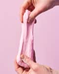 Hands stretching pink edible playdough against a pink background.