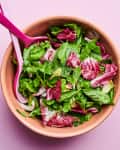 A large bowl of spring greens is mixed with two salad tongs.
