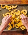 Hands placing Delicata squash on roasting pan.