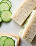 Cucumber sandwiches with cream cheese filling, sliced cucumbers, and white bread on a light surface.