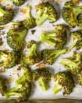Overhead shot of roasted broccoli on white parchment paper, in a sheet pan.
