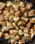 An overhead shot of chicken garlic parmesan bites in a cast iron skillet on a marble surface