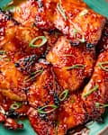 overhead shot of filipino barbecue chicken on s teal plate, topped with green onion