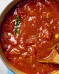 overhead shot marinara in a large pot with a wooden spoon in it