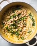 Creamy pasta with white beans and fresh spinach in a pot.