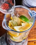 adding some water to a blender filled with lemon and lime slices