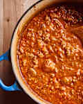 grace parisi's bolognese sits in a pasta pot with a wooden spoon in it