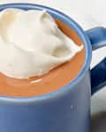 Angled shot of Jacques Torres' hot chocolate recipe in a dark blue mug, topped with whipped cream.
