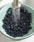 overhead shot of berries getting rinsed in a light blue colander in the sink