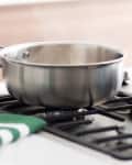 Stainless steel saucepan on a gas stove with a green and white striped towel nearby.