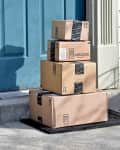 Four stacked Amazon packages on a doorstep with a blue door.