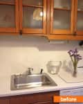 Wooden kitchen cabinets above a stainless steel sink, with a glass pitcher and purple flowers on the counter.