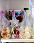 Various marinated chicken pieces in ziplock bags and a container of soup on a refrigerator shelf.