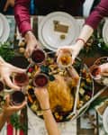People toasting with red wine over a festive table with a roasted turkey, nuts, and greenery.