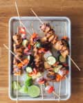 Grilled chicken skewers with zucchini, red peppers, and onions on a baking tray, garnished with lime wedges.